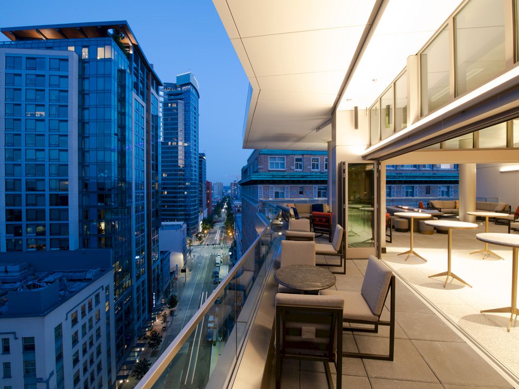 This image shows a modern cityscape viewed from a balcony at dusk, featuring high-rise buildings and an outdoor seating area.