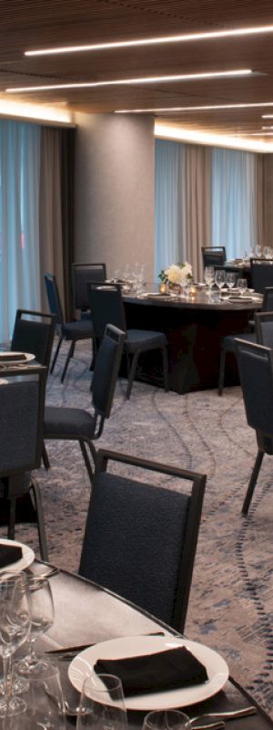 A banquet room set up with round tables and chairs, elegantly arranged with plates, glasses, and napkins for a formal event.