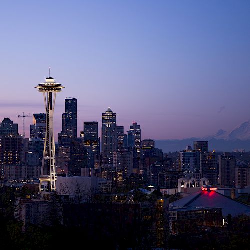 The image depicts the Seattle skyline at dusk, featuring the Space Needle prominently, with Mount Rainier visible in the background.
