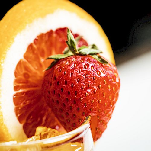 The image shows a close-up of a drink garnished with a slice of citrus fruit and a fresh strawberry, set against a blurred background.