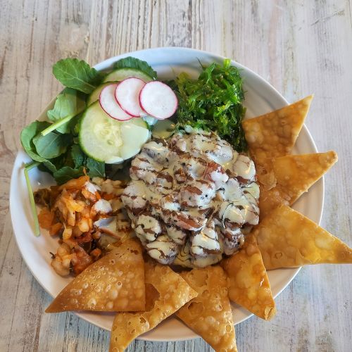 A dish with grilled chicken, tortilla chips, mixed greens, sliced radishes, cucumbers, and diced vegetables on a white plate.